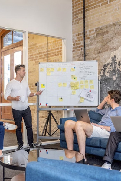 Three men sitting in a casual office, listening to a fourth man present at a whiteboard.
